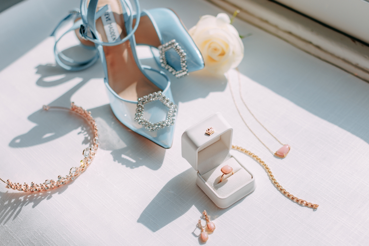 Flatlay of blue Steve Madden bridal shoes with a tiara and pink gemstone jewelry