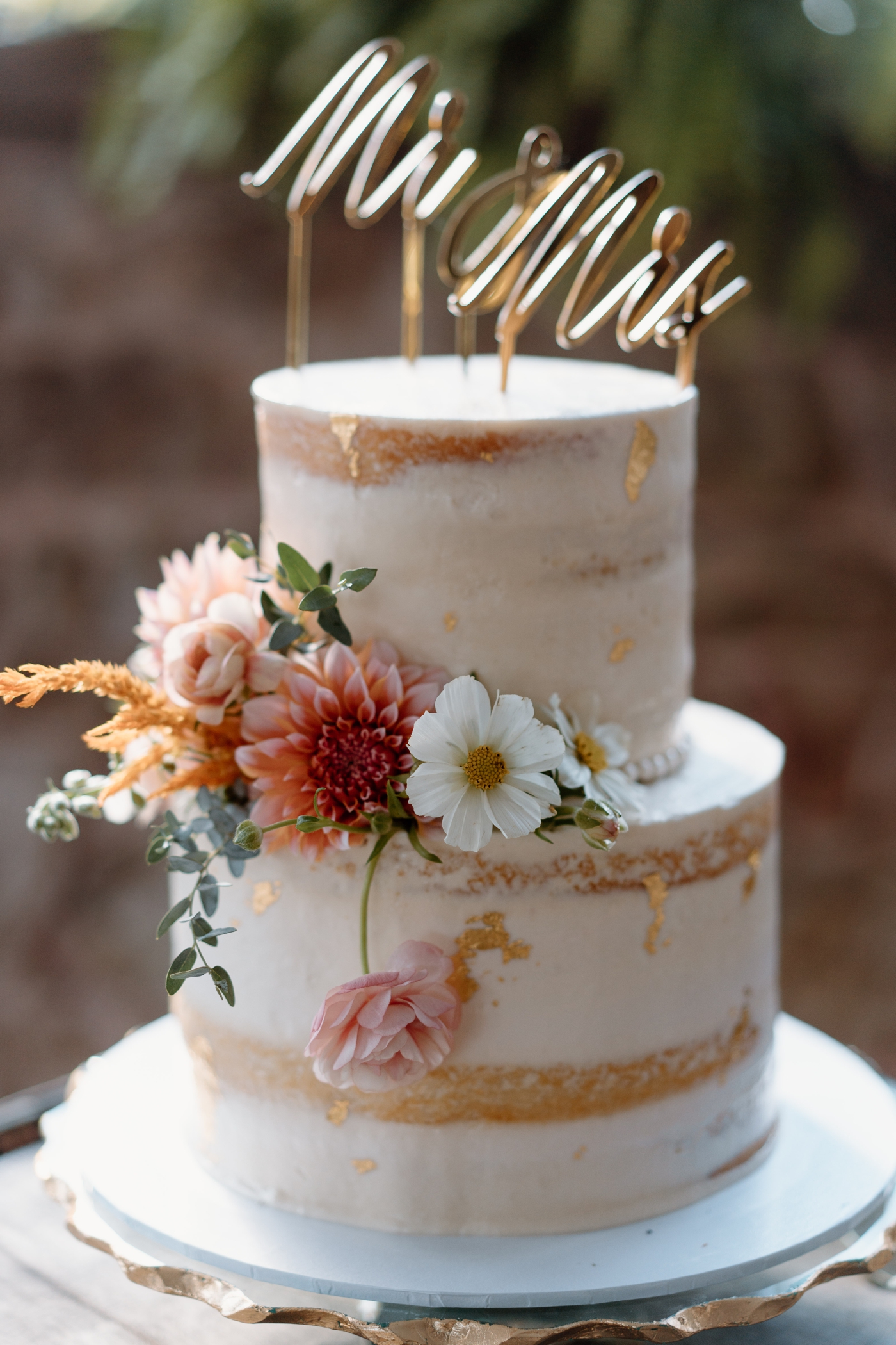 Naked wedding cake decorated with gold leaf and wildflowers